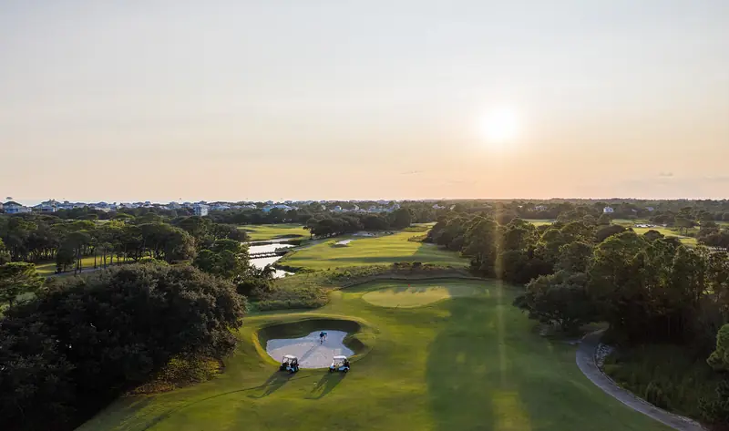Drone shot looking down a coastal fairway toward the setting sun